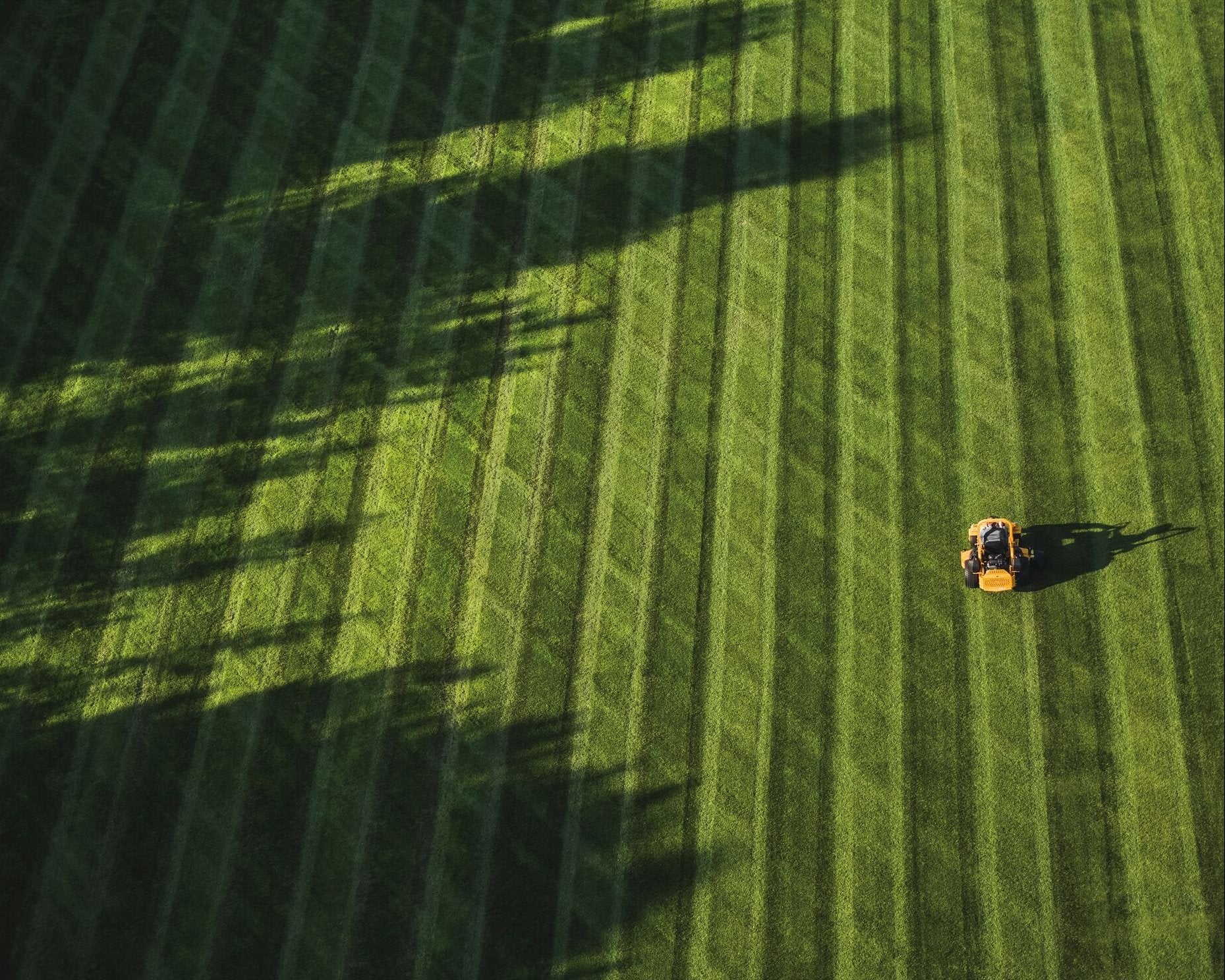 Tractor in a large green field with striped patterns - Country Mower Centre